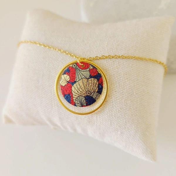 collier-fleurs-or-secondaire-3 Collier doré en acier inoxydable avec pendentif sequin japonais motif Ginkgo posé sur support clair.