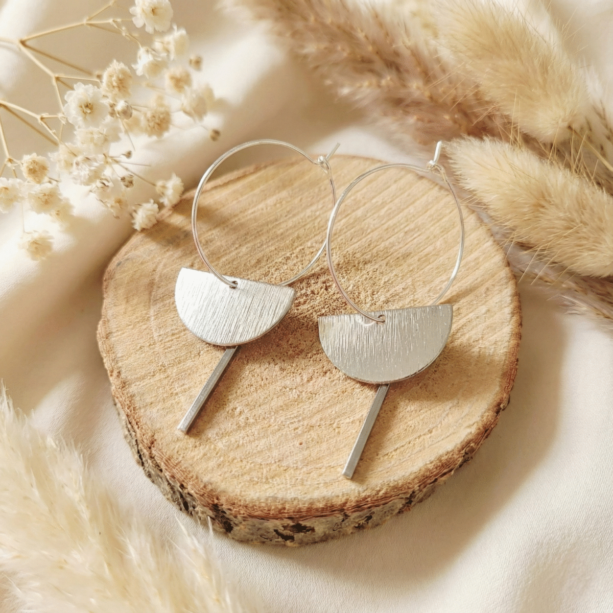 hoto de créoles argentées avec pendentif géométrique demi-lune brossée et barre verticale sur fond bois