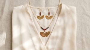 Associer collier et boucles d'oreilles : collier Ginkgo ajouré et boucles Ginkgo Nuit dorées sur un chemisier crème