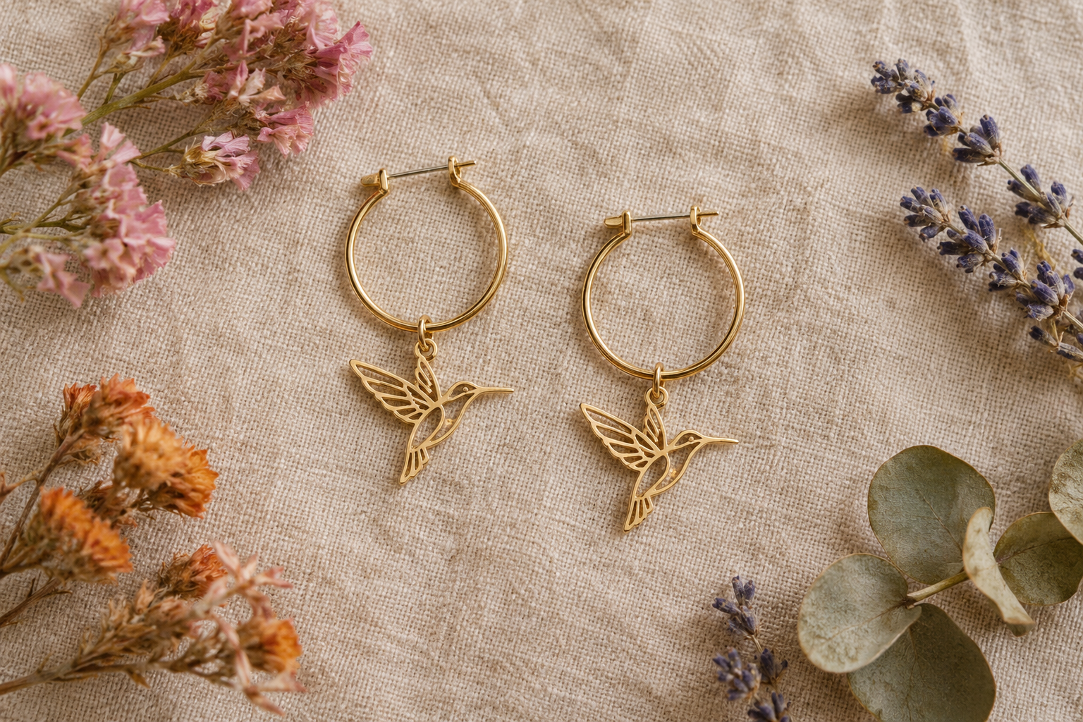 Créoles colibri dorées posées sur du lin, entre des fleurs séchées